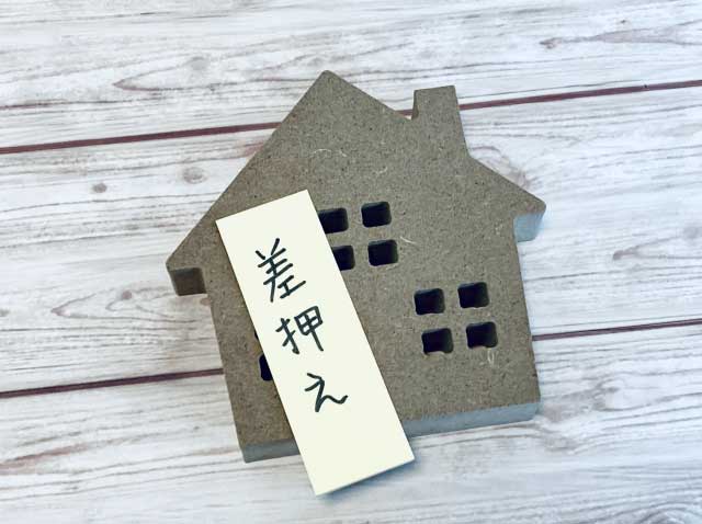 木でできた家の模型と差押えと描かれた札